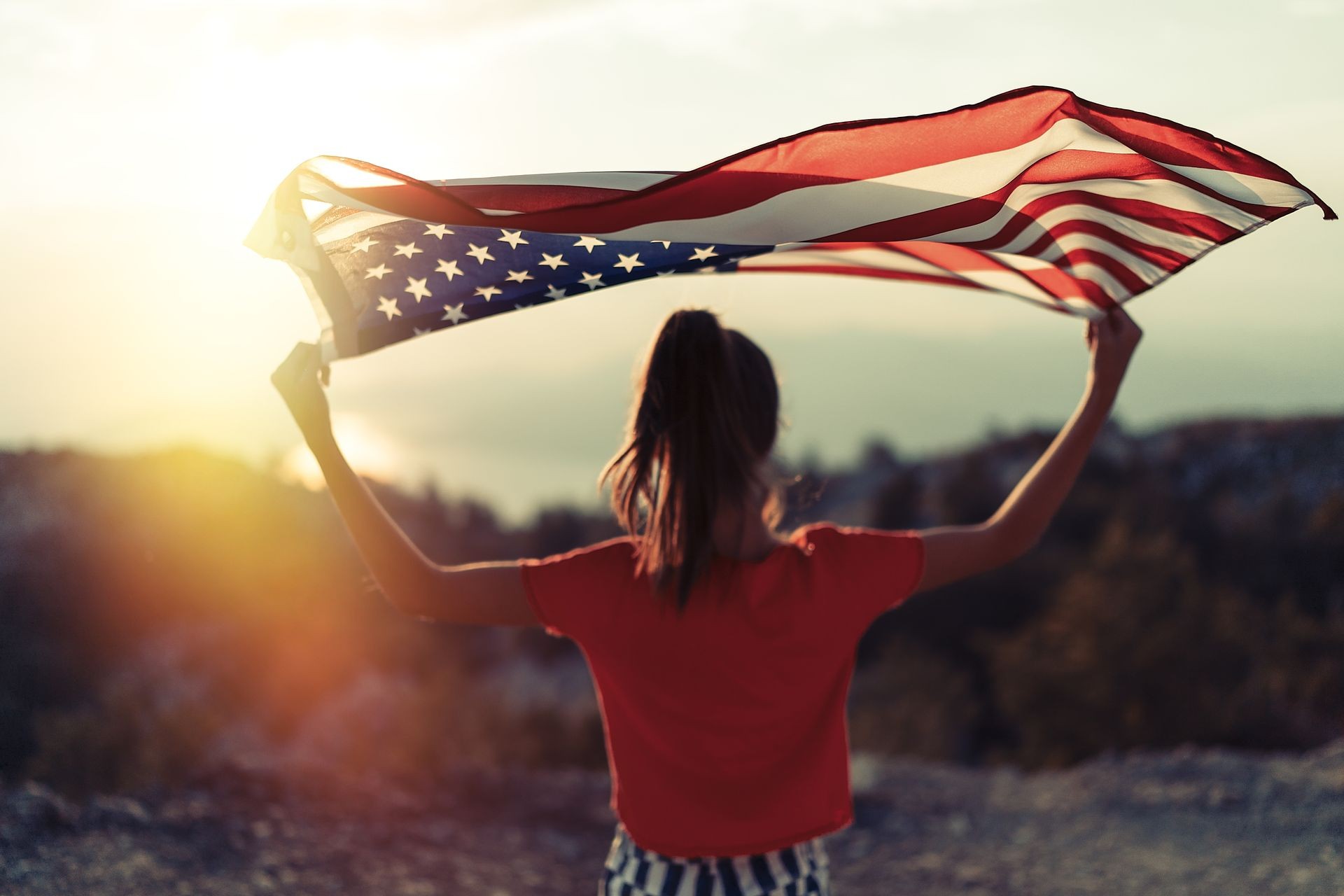 Child girl is waving American flag on top of mountain at sky background. Sunset time. USA resident, US citizen. Immigration concept Child girl is waving American flag on top of mountain at sky background. Sunset time. USA resident, US citizen. Immigration concept